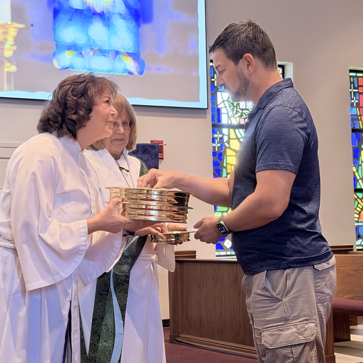 A worshipper taking a small cup from the communion tray held by a server at the front of the Sanctuary