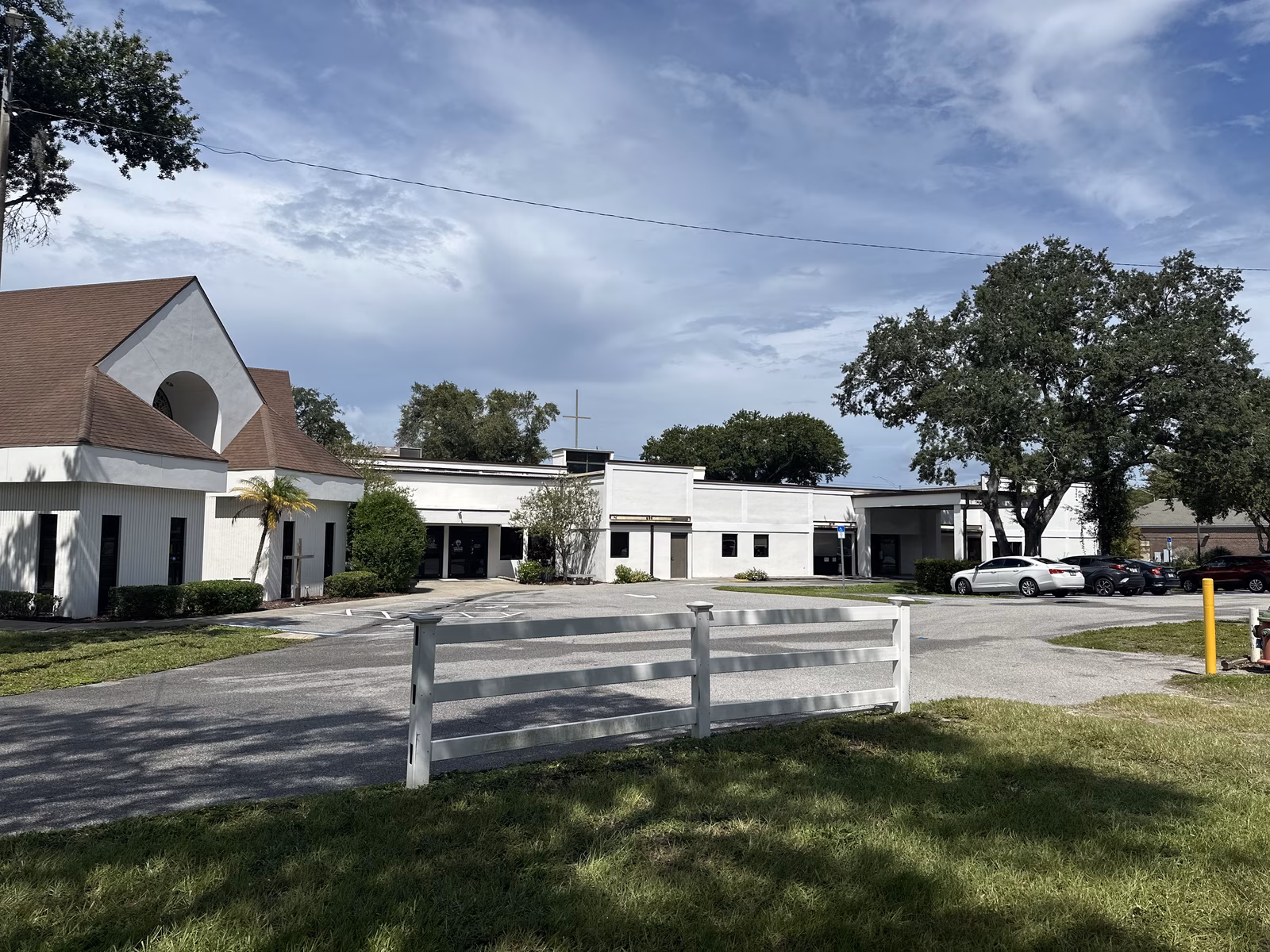 The parking lot looking toward the glass double entrance doors, with the Sanctuary's peaked roof at left and the rooftop cross behind