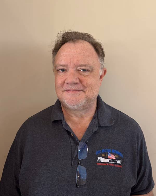 David Vickers, smiling, with short greying hair and a dark grey polo shirt, sunglasses hooked at the collar.