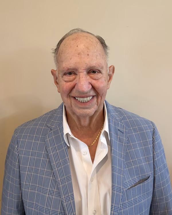 Mike Milo, smiling, wearing a pale blue plaid blazer over an open-collared white shirt.