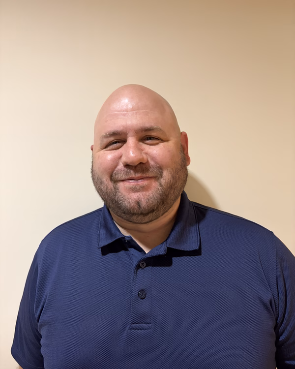 Vito Corti, smiling, with a shaved head and short beard, wearing a navy polo shirt.